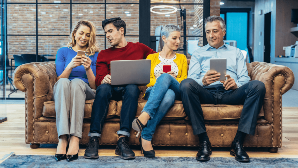 four people sitting on a sofa and looking at their electronical devices