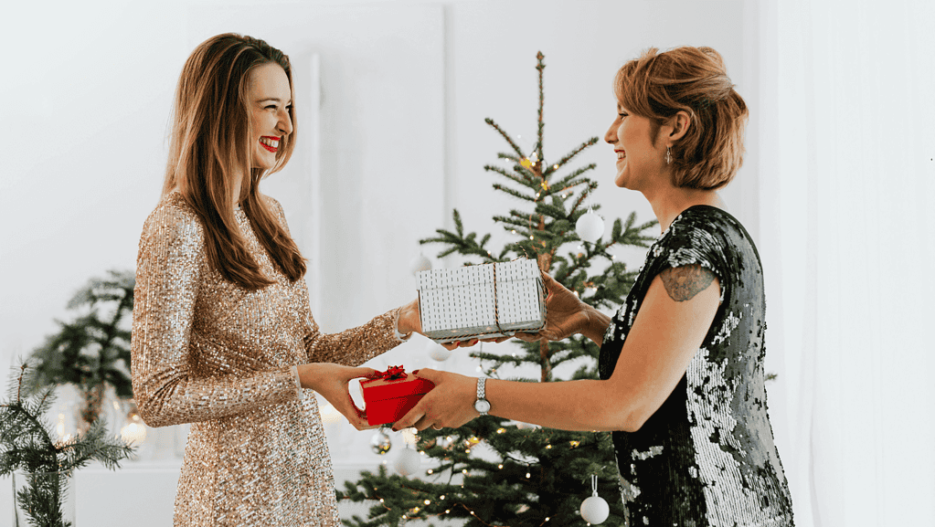 Two women exchanging gifts while smiling with each other.